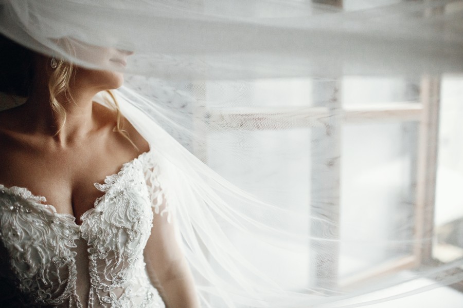 veil-covers-bride-s-face-while-she-stands-before-window.jpg