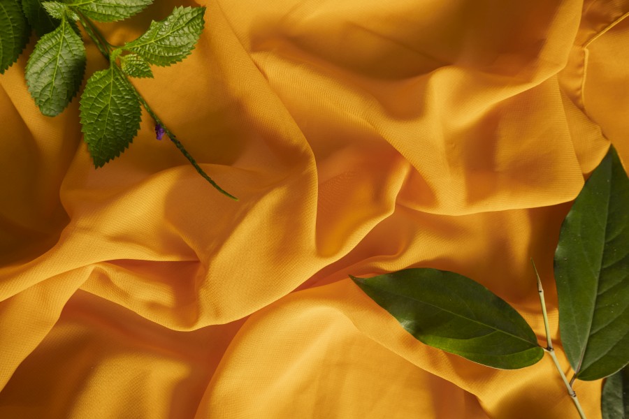 summer-concept-yellow-scarf-fabric-texture-background-green-leaves.jpg